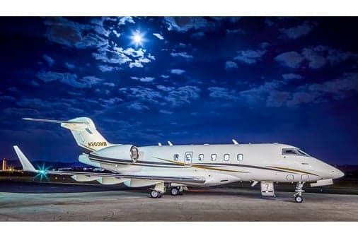 A white business jet with dark and gold stripes, registration N300NB, parked on a tarmac at night under a full moon.