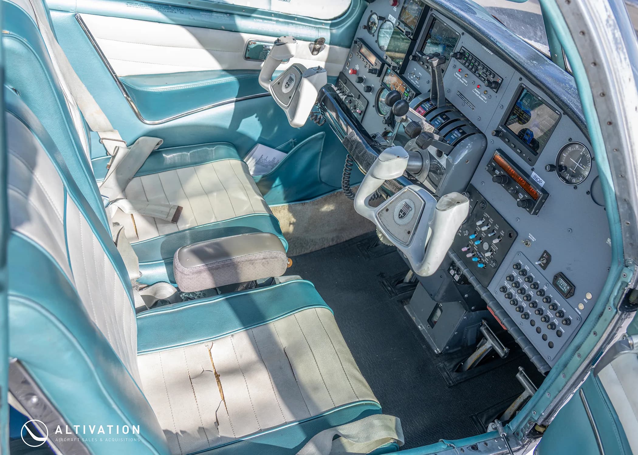 The interior of an aircraft cabin with teal and white seats, looking towards the cockpit.