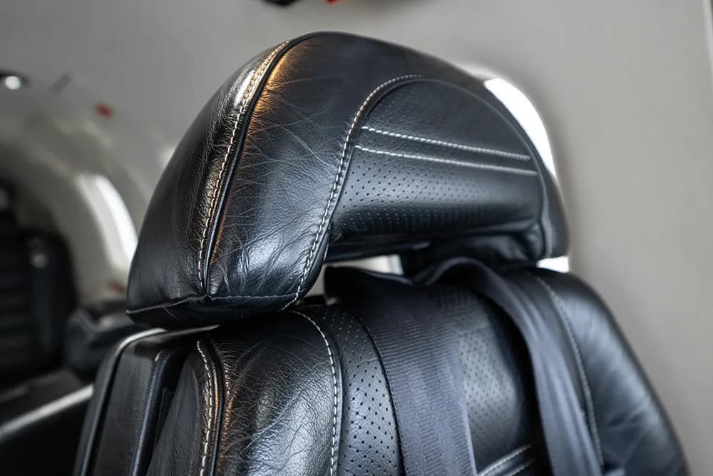 A close-up of a black leather aircraft seat headrest with white stitching.