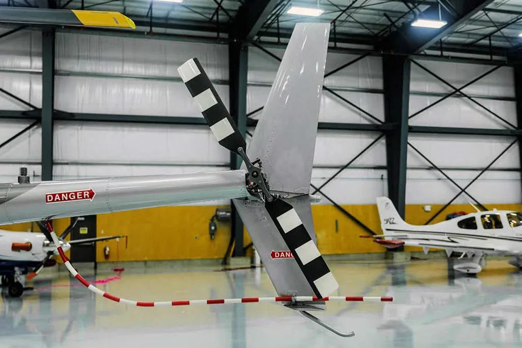 A close-up view of the tail rotor and boom of a grey helicopter with "DANGER" text, inside a hangar.