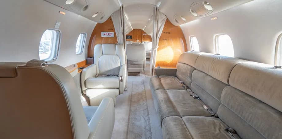The interior of a private jet cabin, looking towards the rear, with a long sofa on the right and individual seats on the left.