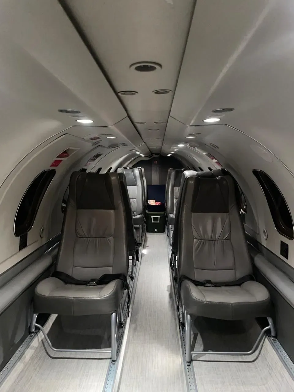 A long view of the aircraft interior cabin, featuring multiple rows of grey leather seats along a central aisle.