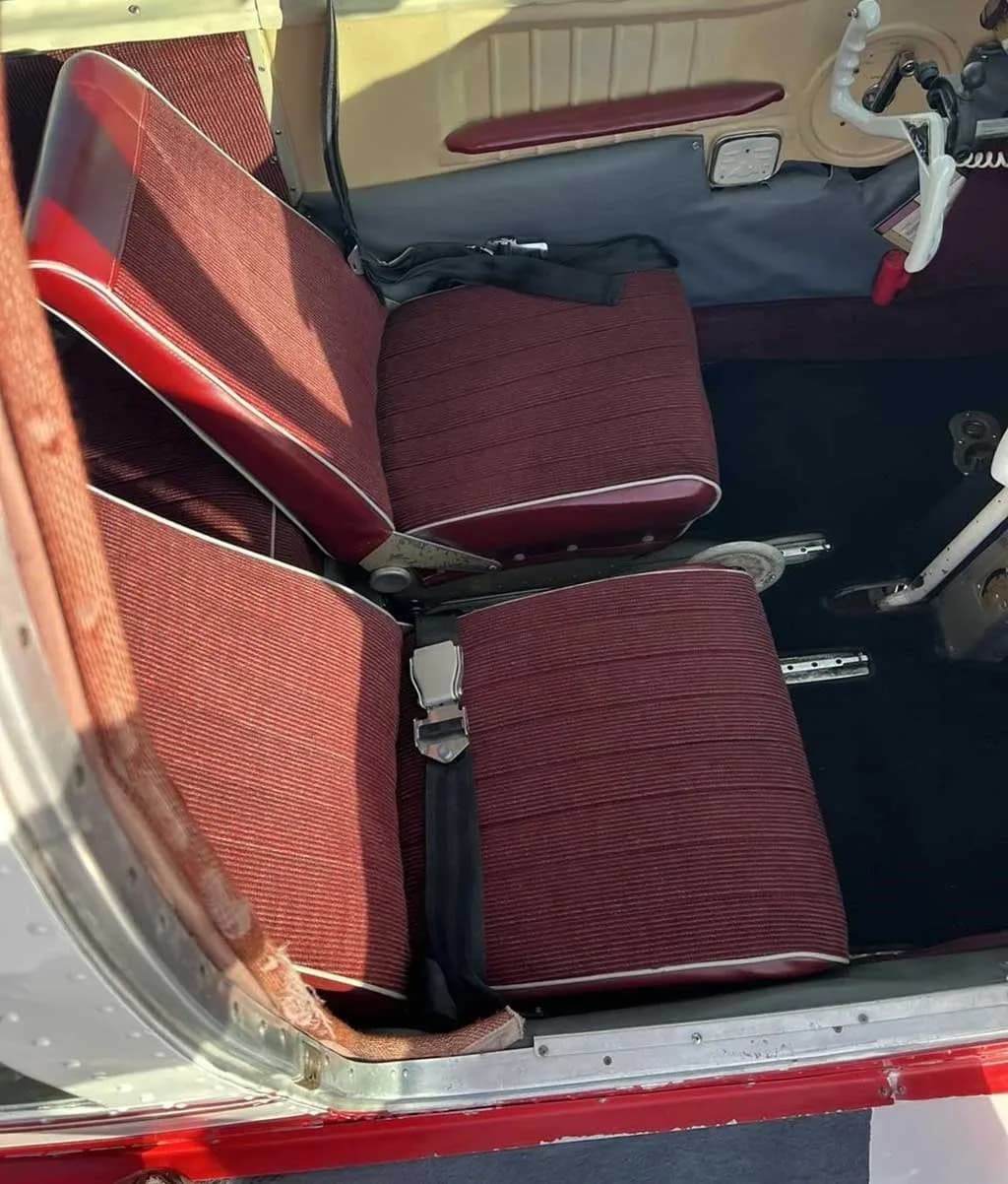 A close-up view of the red striped fabric seats in the aircraft cabin, with seatbelts visible.