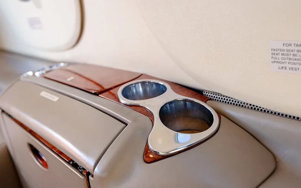 A close-up of a beige side console with two chrome cup holders and wood accents in the aircraft cabin.