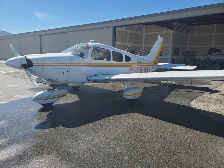 Side view of a white and yellow Piper Archer II aircraft parked on the tarmac.