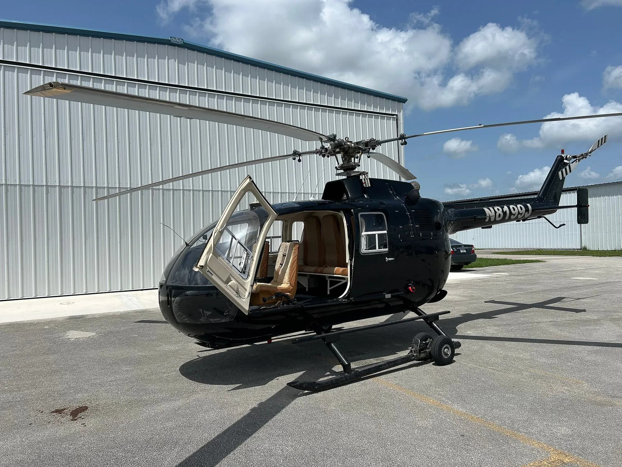 A black helicopter with tail number N8199J and an open door sits on the tarmac.