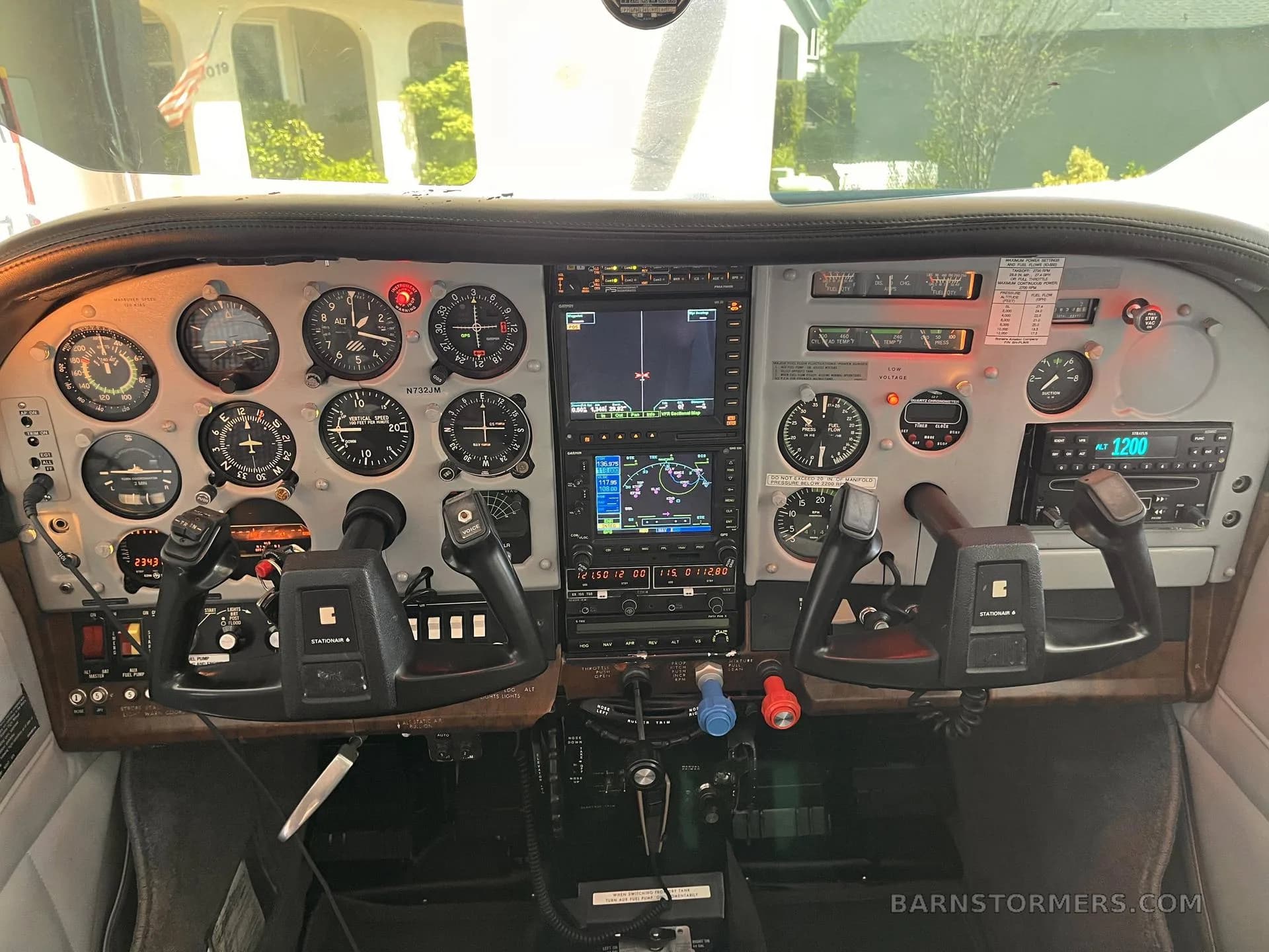 The cockpit of a Cessna aircraft showing the instrument panel with analog gauges, two Garmin GNS units, and dual yokes.