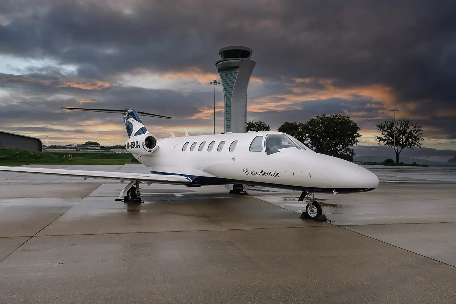 A Cessna Citation CJ2 aircraft with registration D-ISUN parked on the tarmac with an airport control tower in the background.