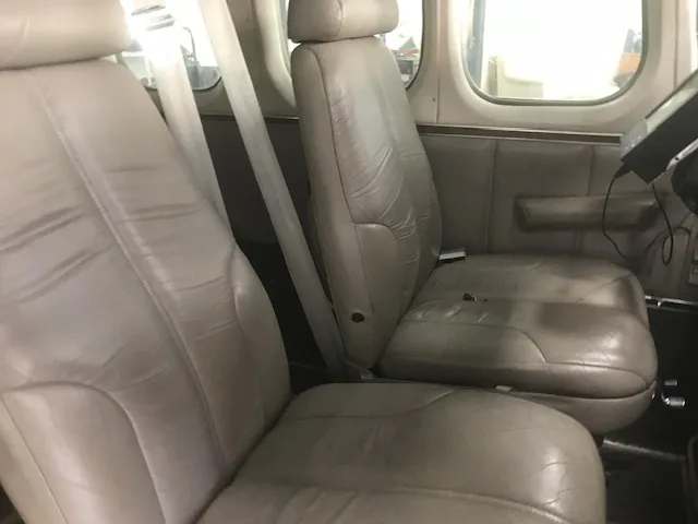 Two light gray leather aircraft seats in the cabin, with seatbelts visible.