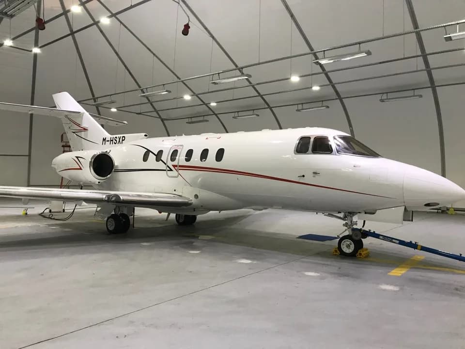 Side view of a white aircraft with red stripes inside a hangar.