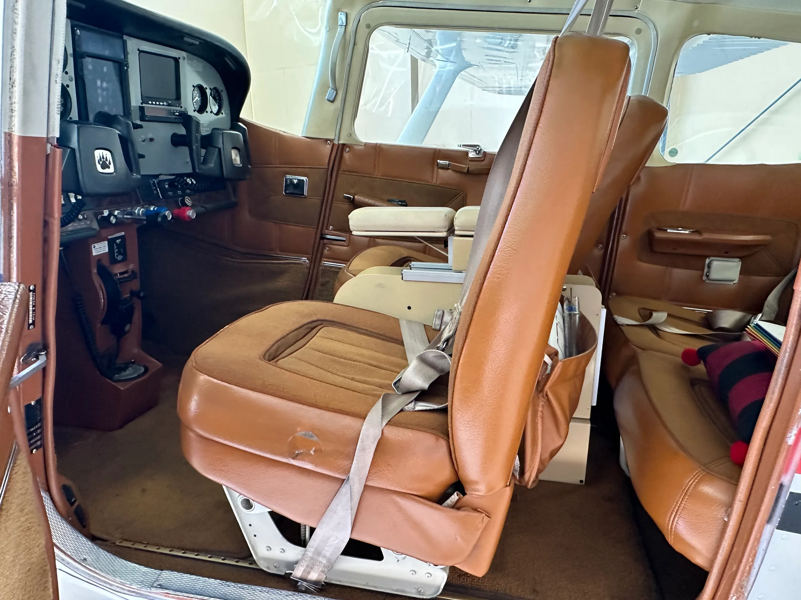 The brown leather interior cabin of a small aircraft, showing the front passenger seat and a glimpse of the cockpit.