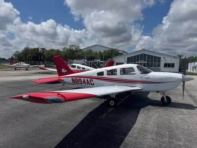 A side view of a white Piper Archer TX with red stripes and tail, registration N894AC, parked on an airport tarmac.