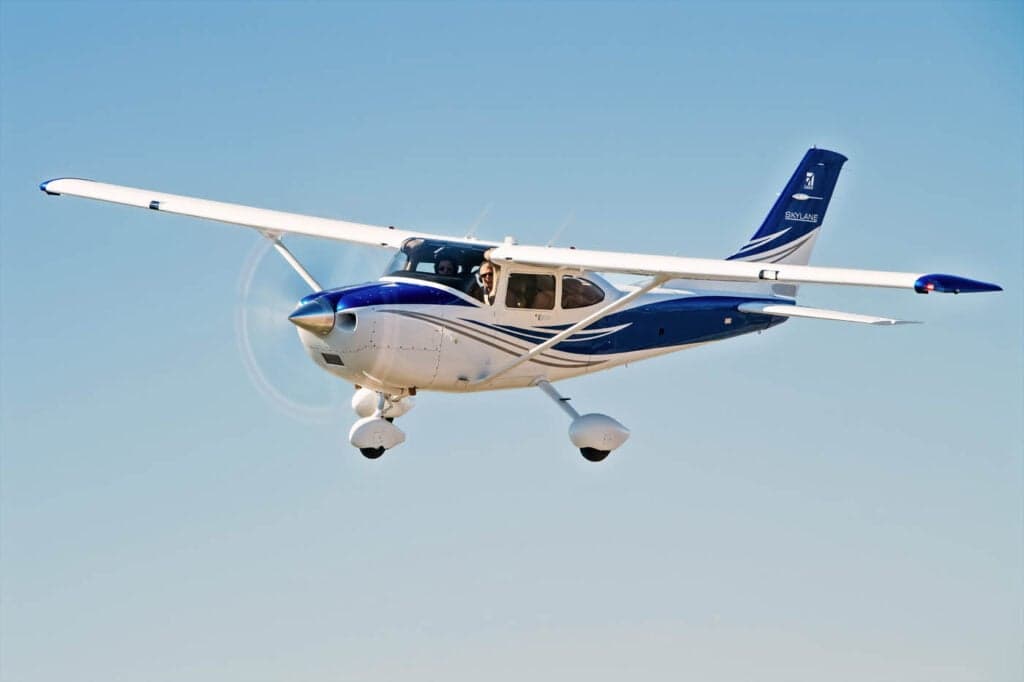 A Cessna Skylane in flight against a blue sky.
