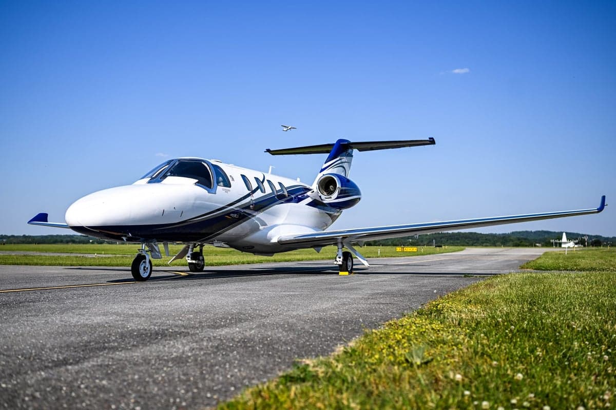 A white and blue Cessna Citation M2 jet on an airport tarmac under a clear blue sky.