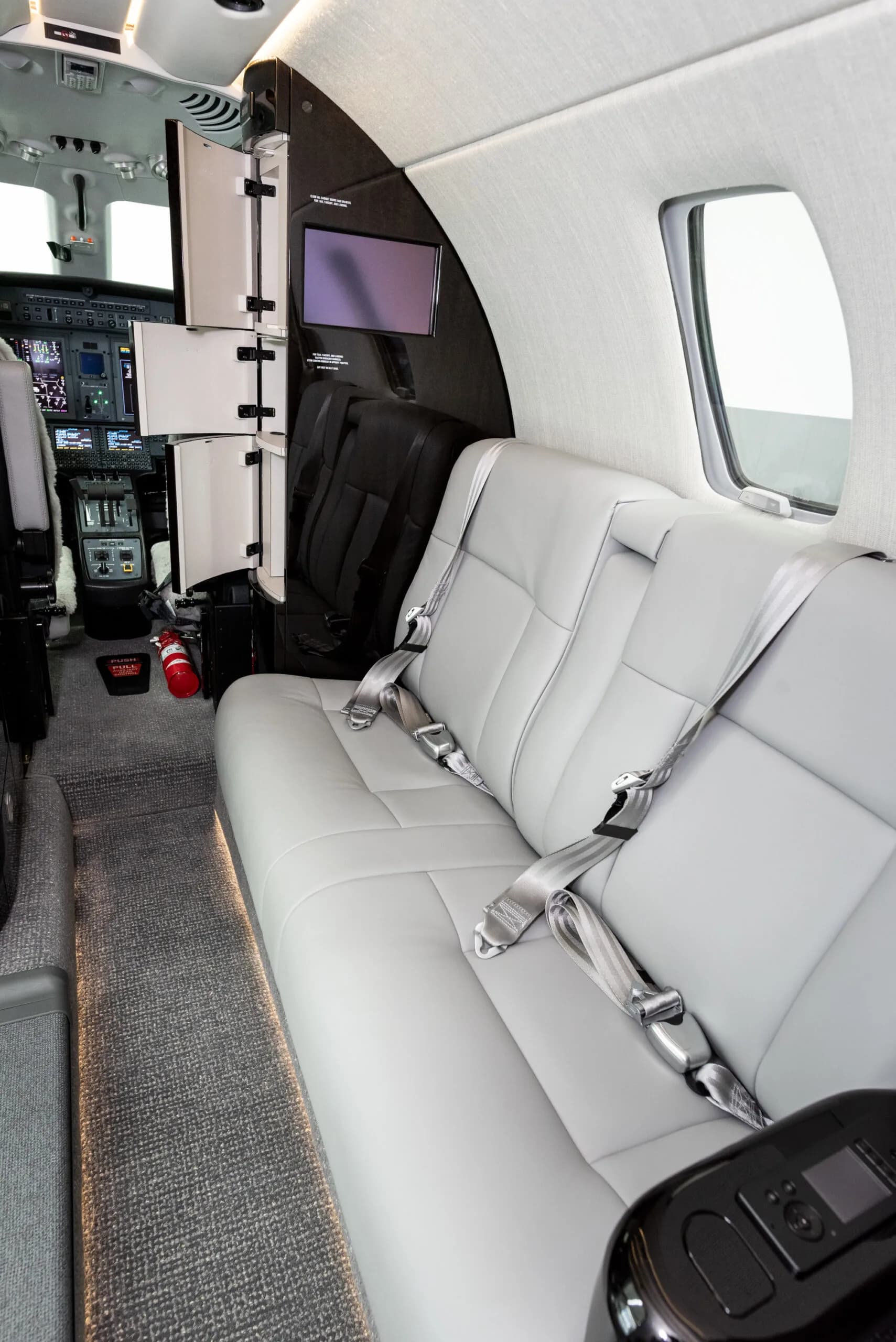 View from the rear of the private jet cabin looking forward, showing a bench seat and the cockpit entrance.