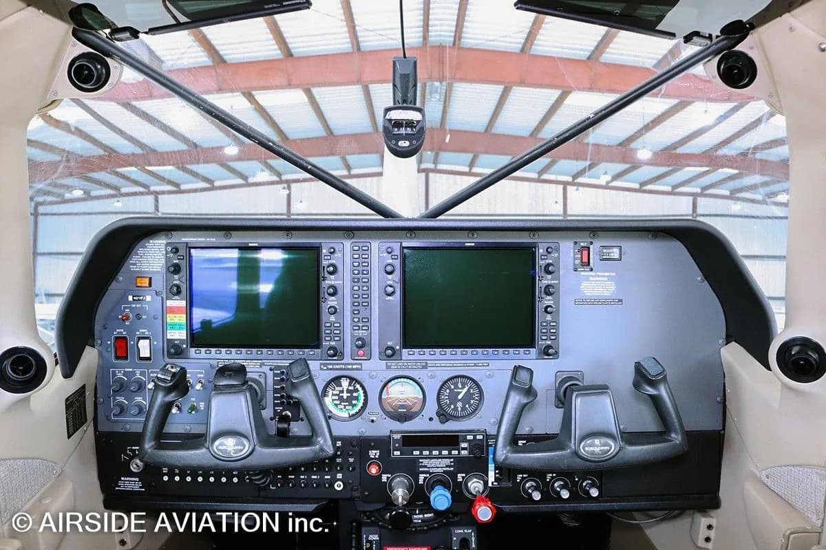 A wide view of an aircraft cockpit with dual large display screens and control yokes.