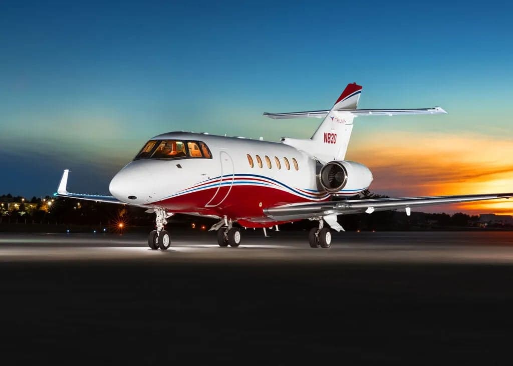A Falcon aircraft with red and white paint scheme is parked on the tarmac at dusk.