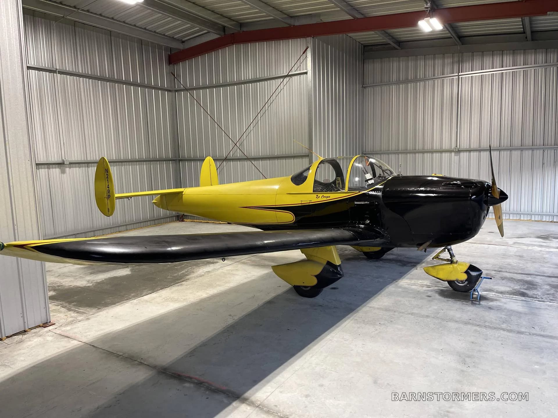 A black and yellow single-engine aircraft with "Le Croco" written on its side, parked inside a metal hangar.