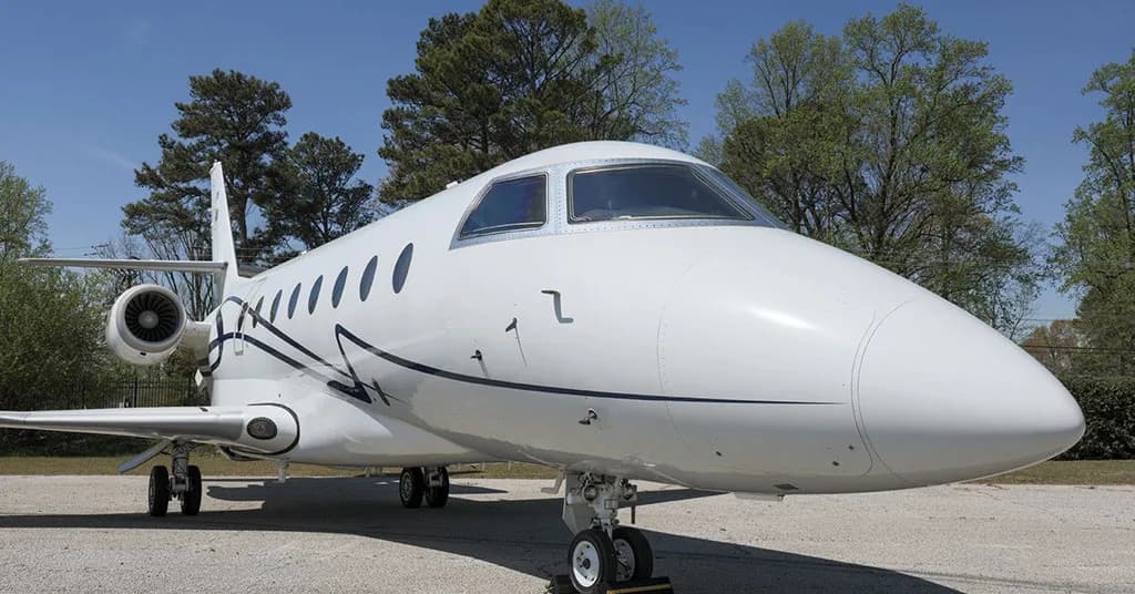 A close-up front view of a white business jet with blue accents, parked outdoors under a clear sky.