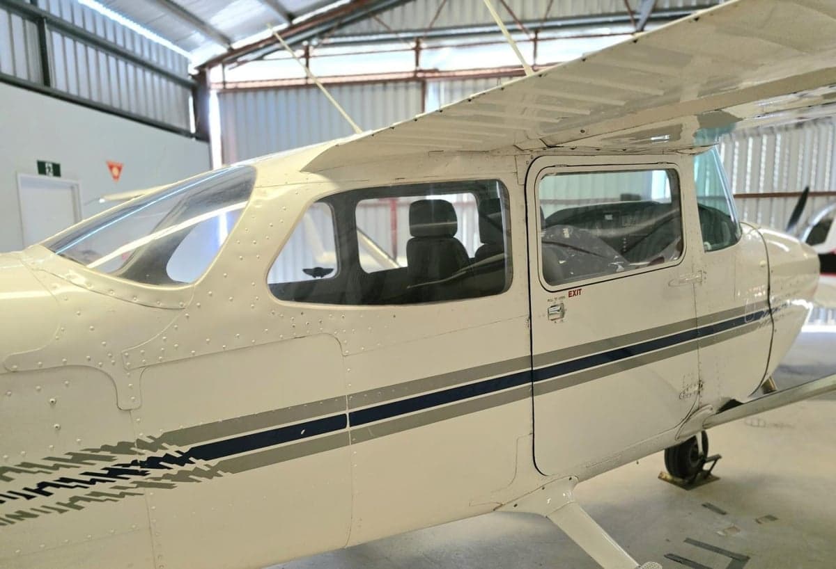 A Cessna aircraft is parked inside a hangar, showing the side and cabin windows.