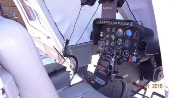 The cockpit of a helicopter with a light-colored seat and a detailed instrument panel.