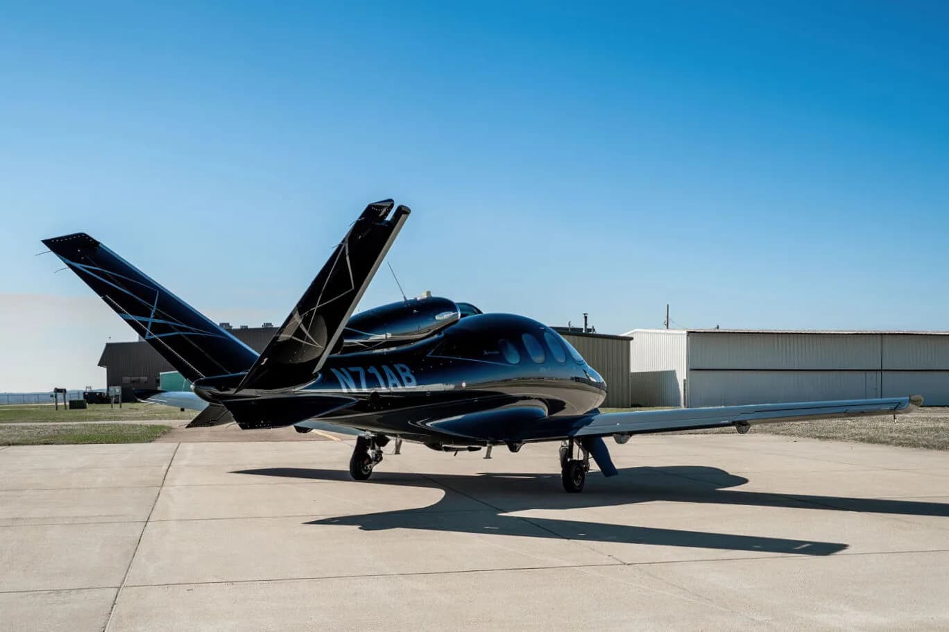 Three-quarter rear view of a black Cirrus Vision Jet (N71AB) with a geometric tail design, parked on an airport tarmac.