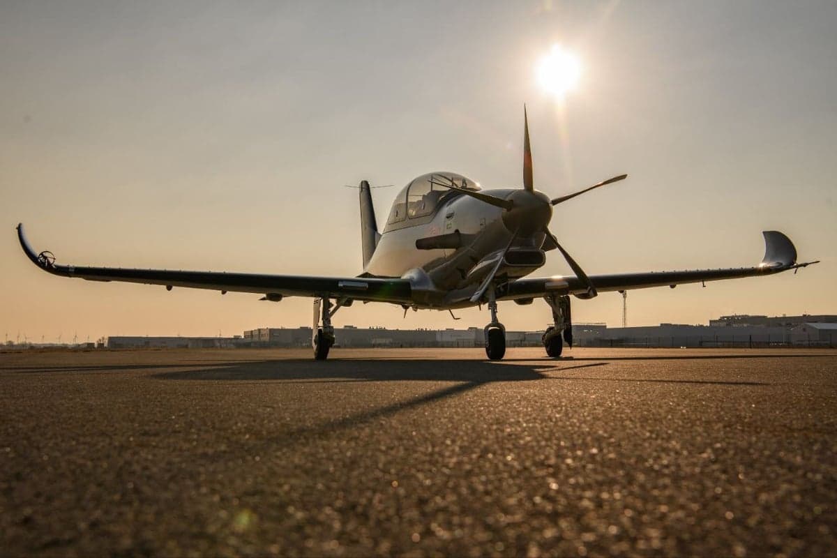 A silver CEAD aircraft sits on the tarmac at sunset.