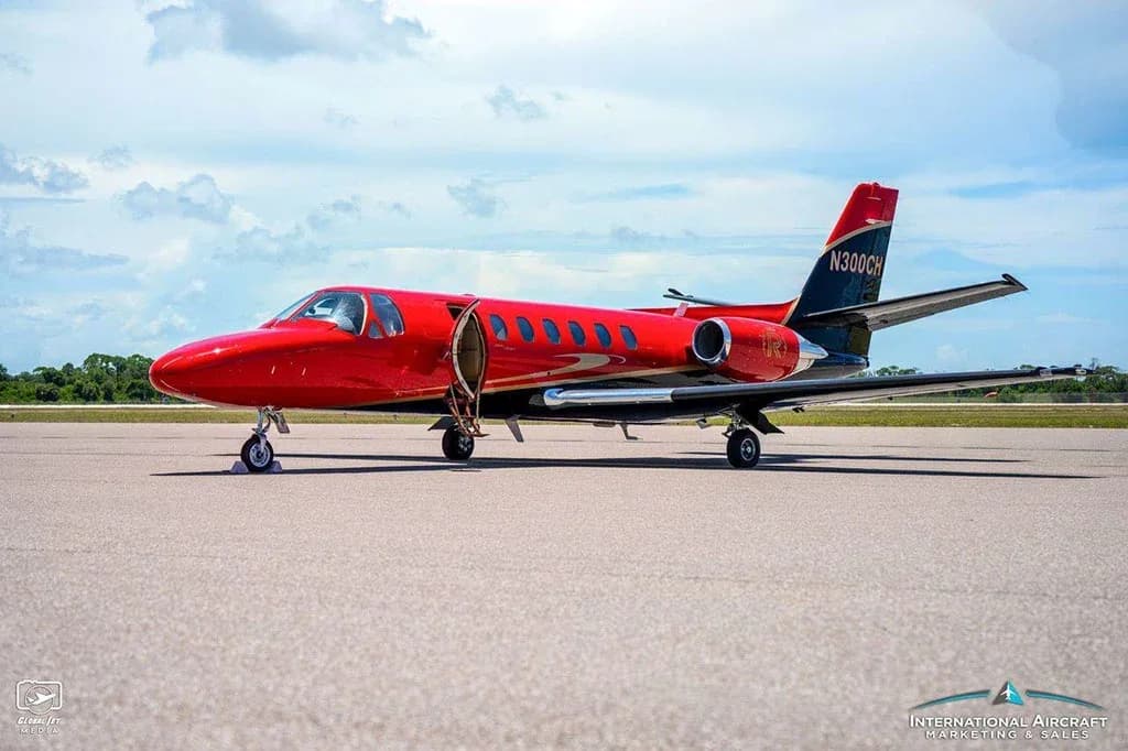 A red and black Cessna Citation V (N300CH) jet sits on a tarmac with its main cabin door open.
