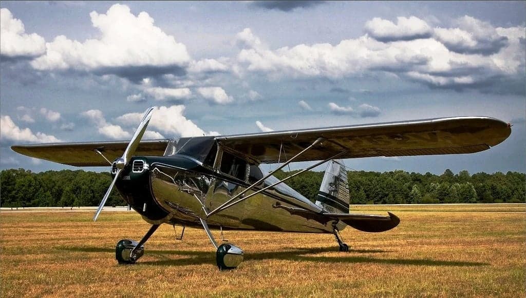 A Cessna 170 aircraft is parked on a grassy field under a cloudy sky.