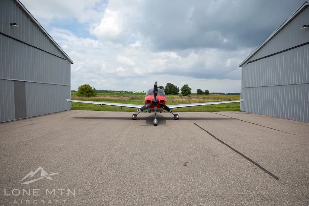 A red and silver Cirrus SR22 aircraft, N521P, parked head-on between two hangars.
