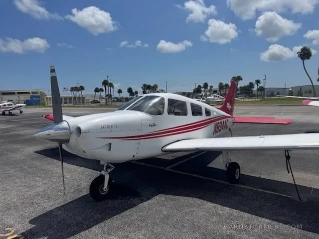 A front-left view of a white Piper Archer TX with red stripes and tail, registration N894AC, parked on an airport tarmac.