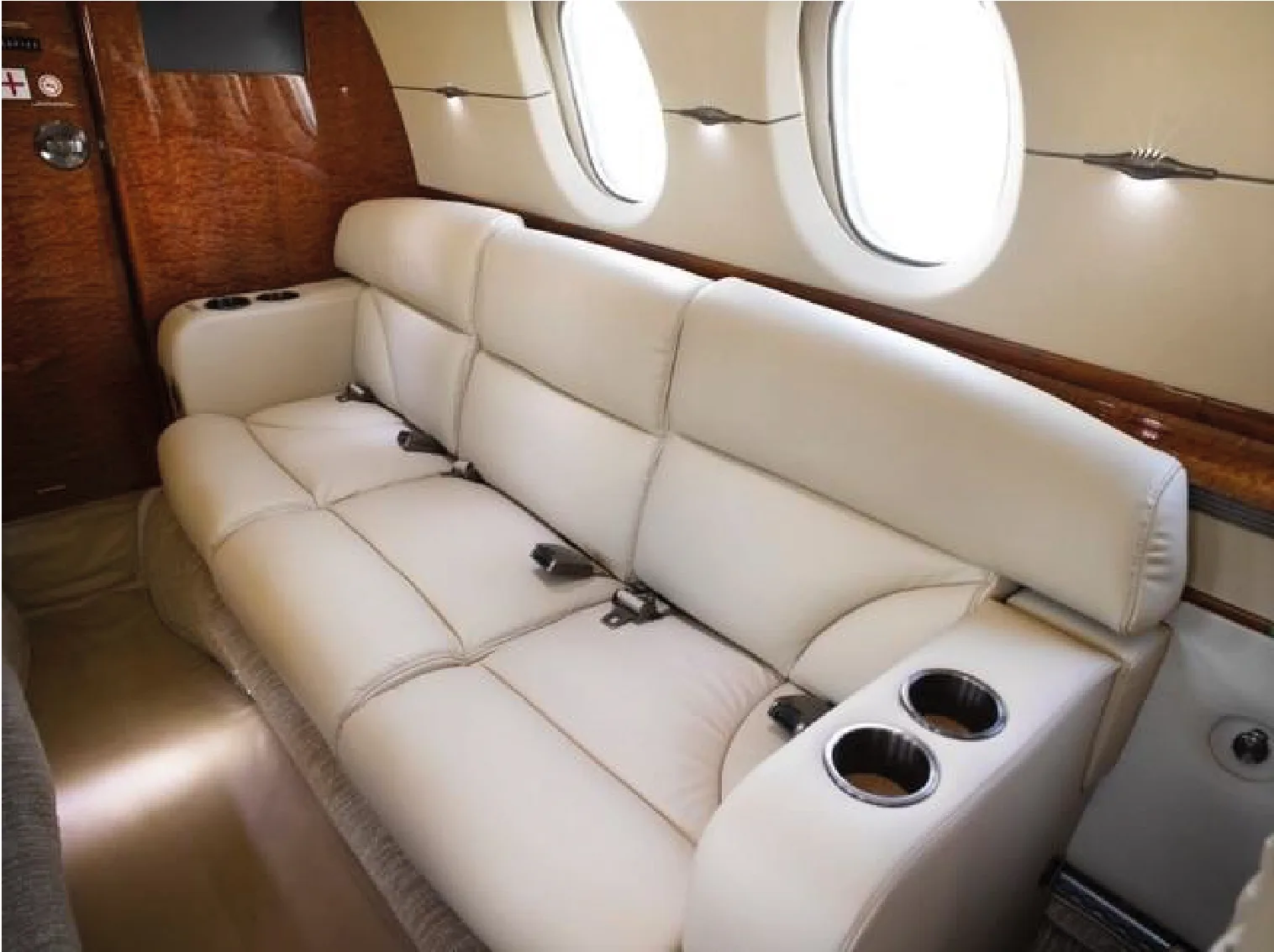 Aircraft interior with cream-colored leather sofa and wood trim.