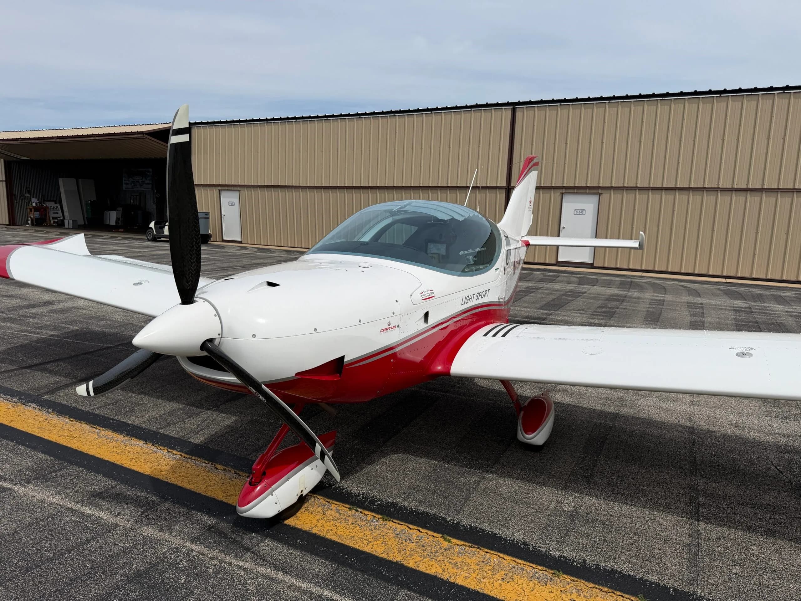 A three-quarter front view of the white and red SportCruiser aircraft N574SC parked on an airport tarmac.