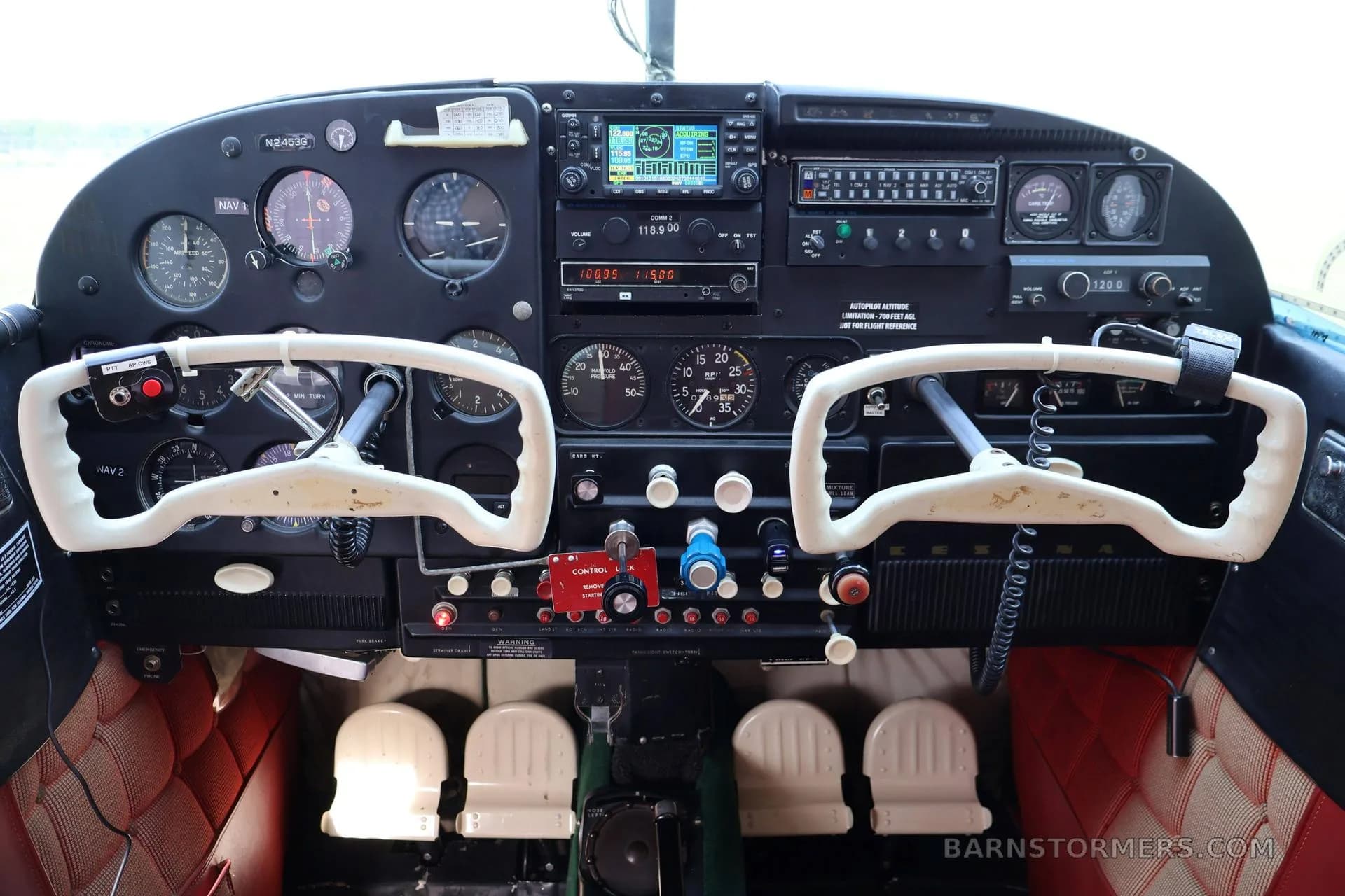 The cockpit of a small aircraft features a black instrument panel with various gauges, radios, and two white control yokes.