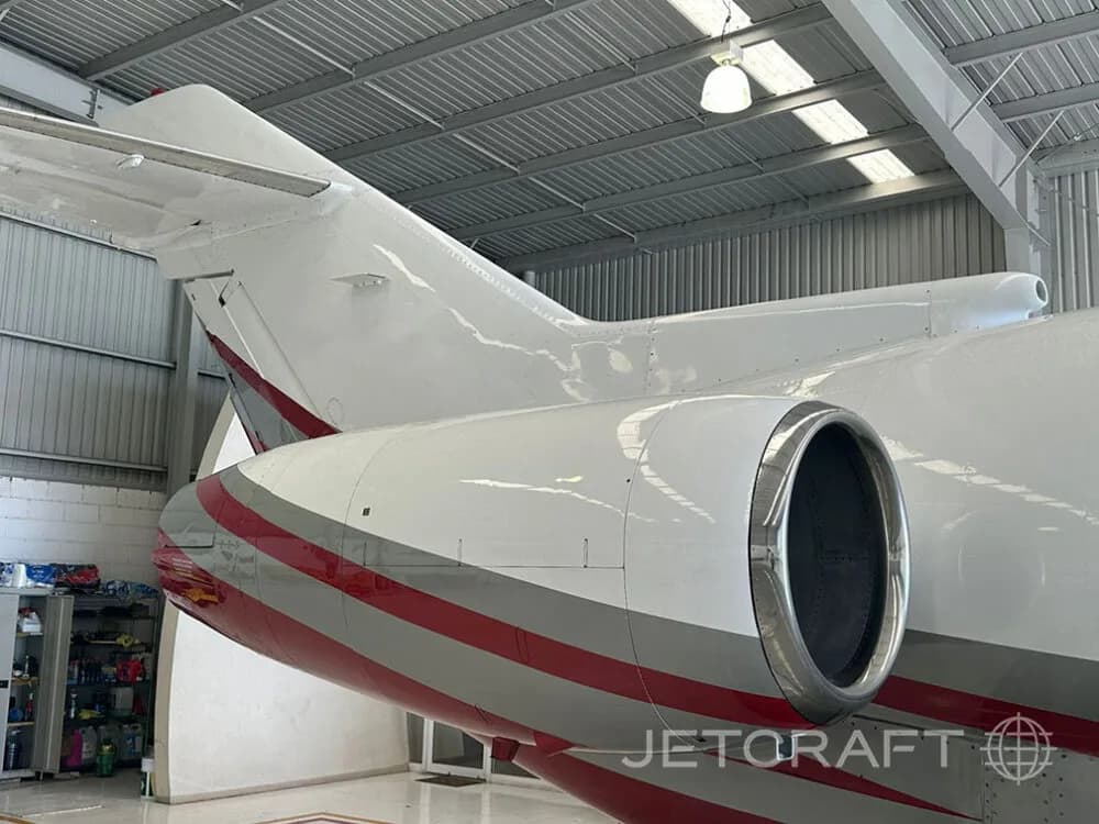 A close-up view of the tail and engine of a white and red business jet inside a hangar.