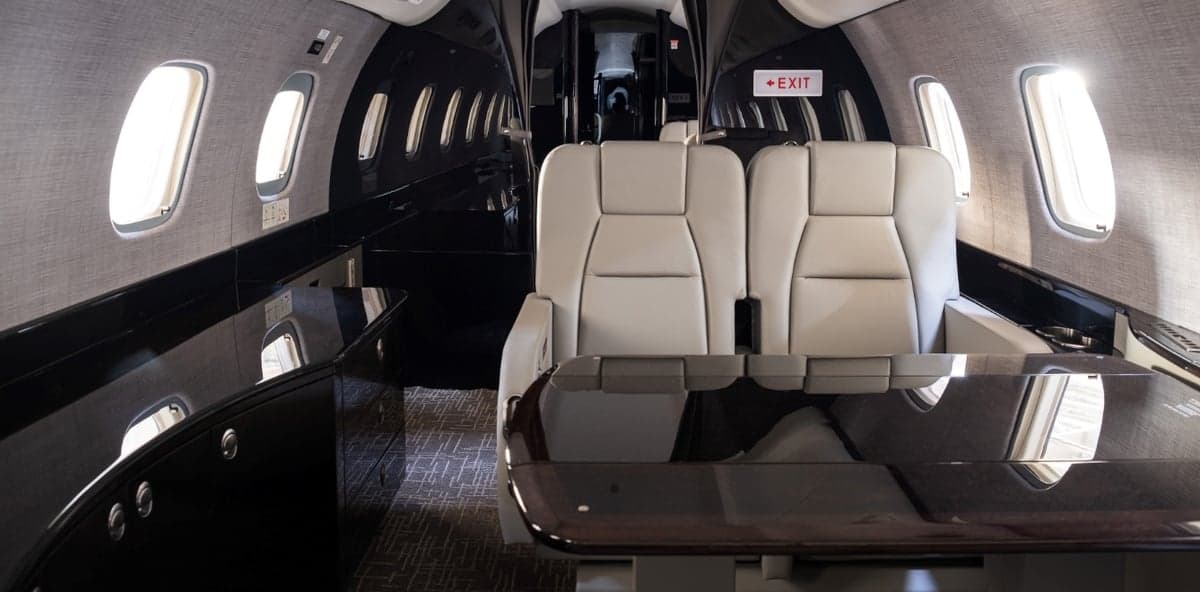 View of the aircraft cabin with gray leather seats and a dark wood table.