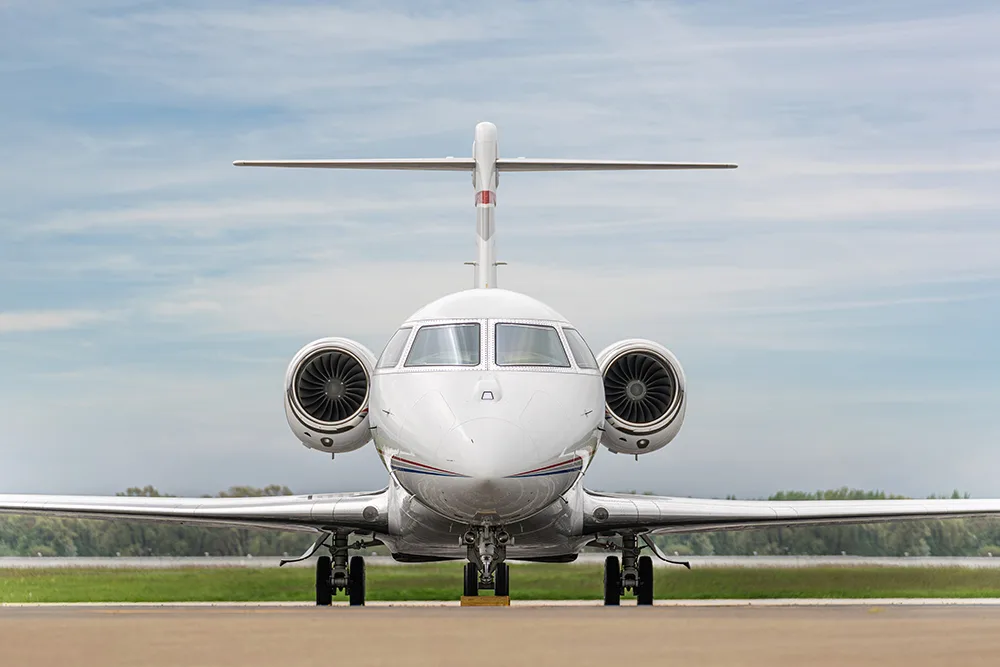 A head-on view of a white business jet with twin engines on the rear fuselage, parked on an airfield.