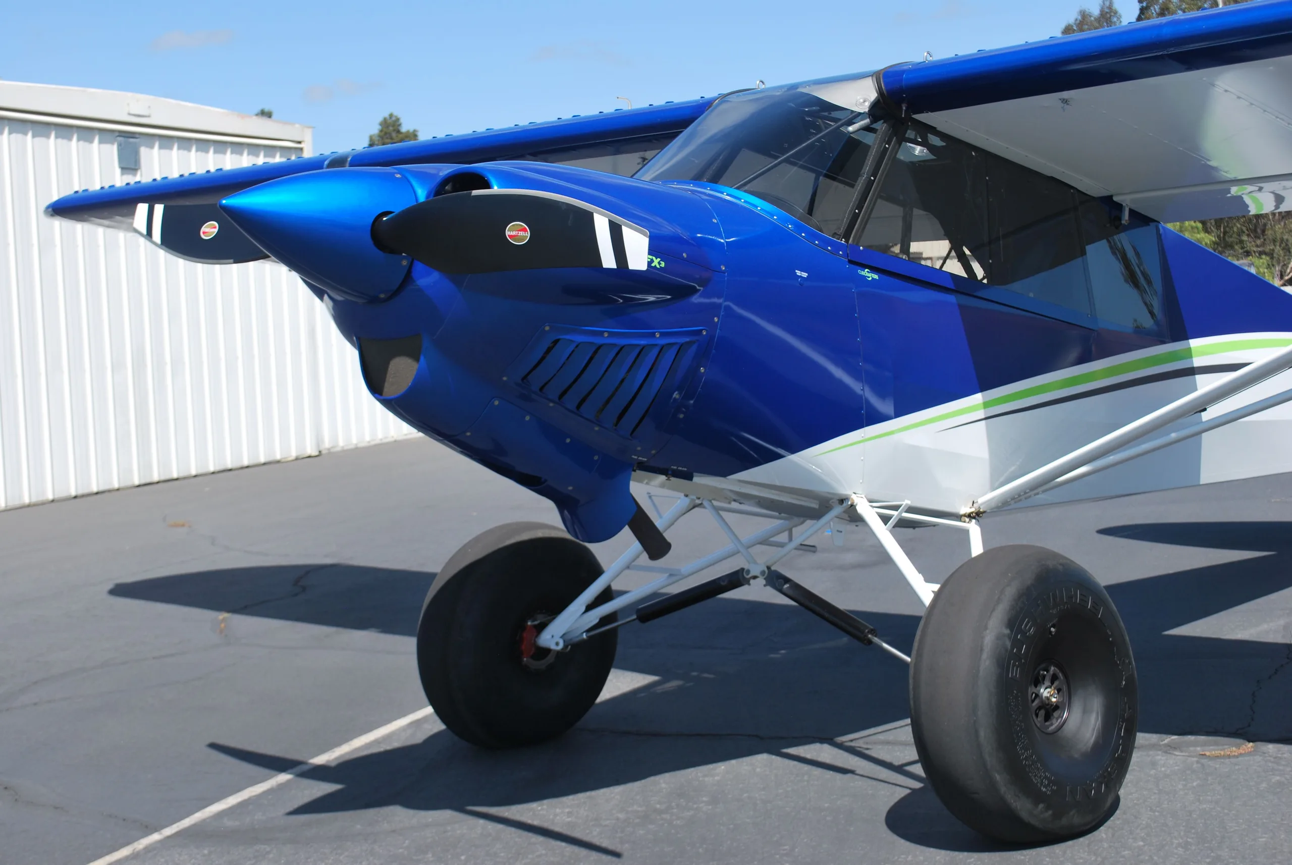 A close-up view of the blue nose and propeller of a Carbon Cub FX3 aircraft with large tires.