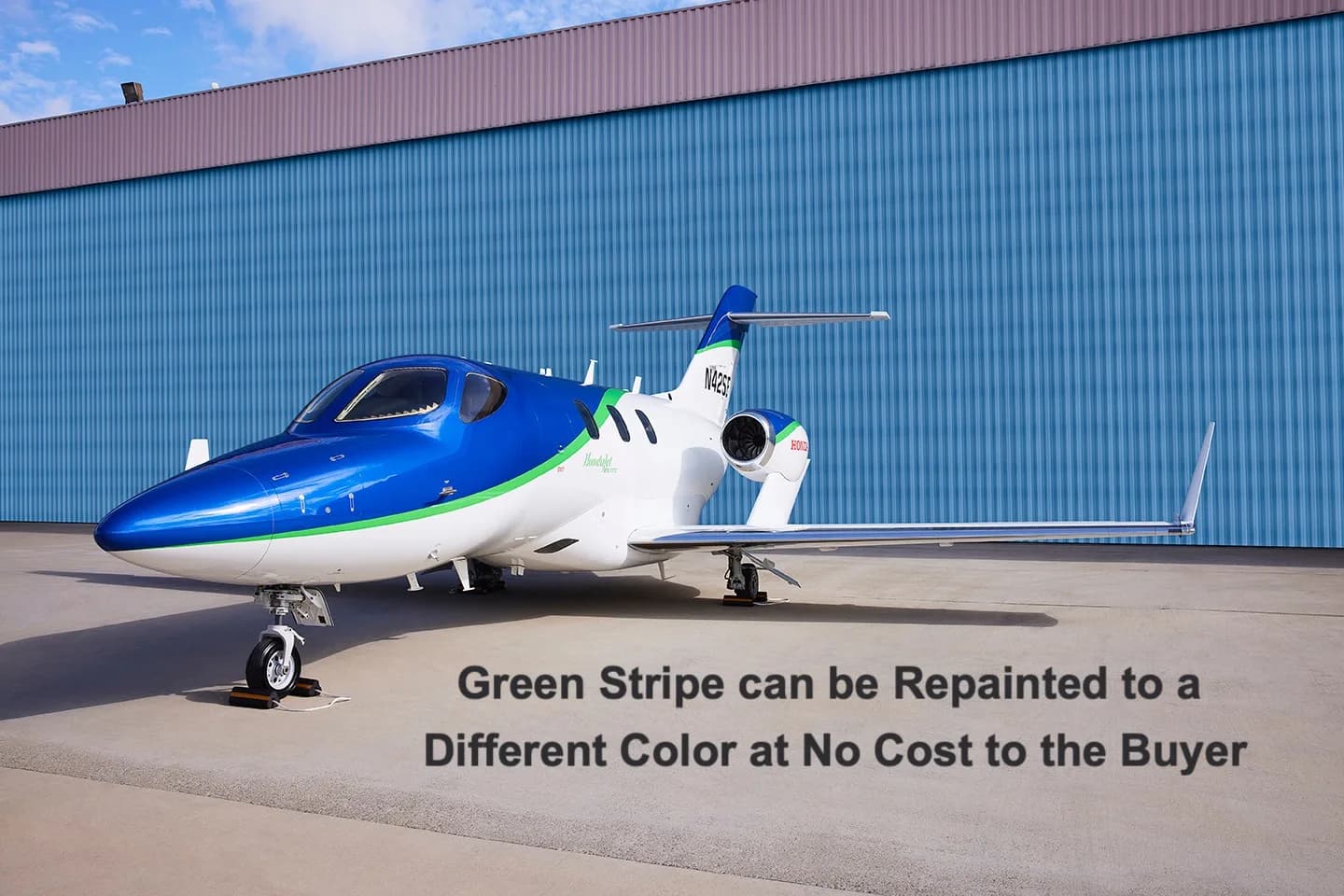 A white and blue HondaJet Elite with a green stripe, registration N42SE, parked on an airfield with a blue hangar in the background.