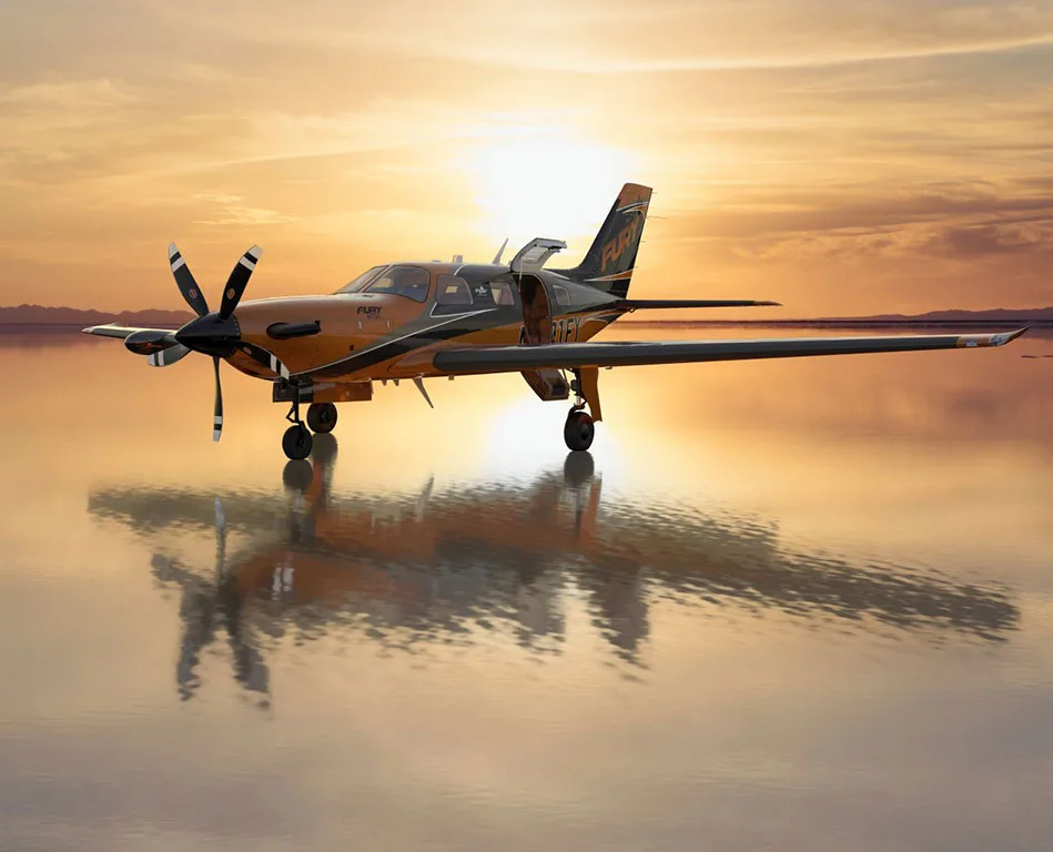 A bronze and black single-engine turboprop aircraft (N701FY) with 'FURY' on the tail, parked on a reflective surface at sunset.