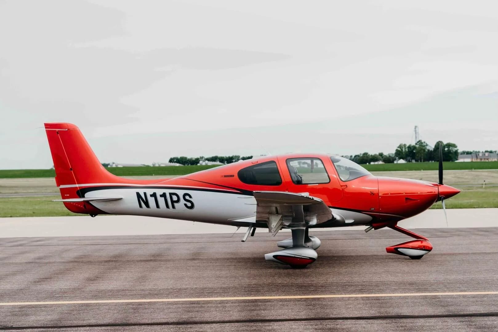 A red and silver Cirrus SR20 Premium aircraft (N11PS) parked on an airfield tarmac.