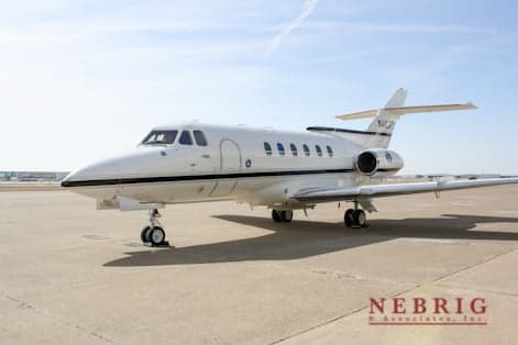 A white Hawker 800XP business jet with a dark stripe is parked on an airport tarmac.
