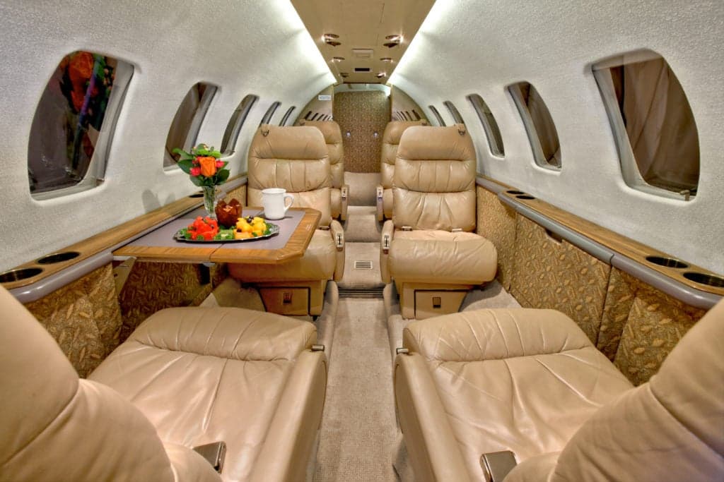 Spacious Citation Ultra cabin with tan leather seats and a table with refreshments.