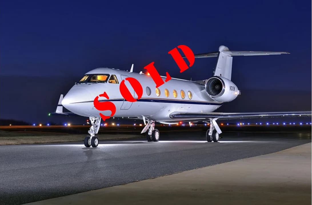 A white Gulfstream business jet with "SOLD" text, parked on an illuminated airfield at night.