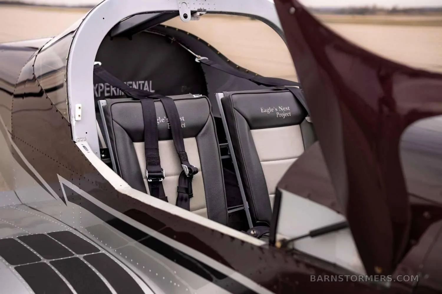 A view into the open canopy of the aircraft, showing two black and tan leather seats with "Eagle's Nest Project" embroidered on them.