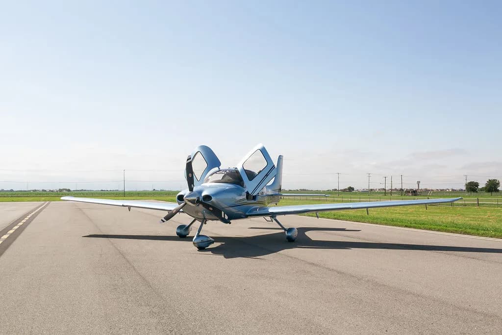 A wide shot of the light blue Cirrus SR22 aircraft with its gull-wing doors open on an airfield.
