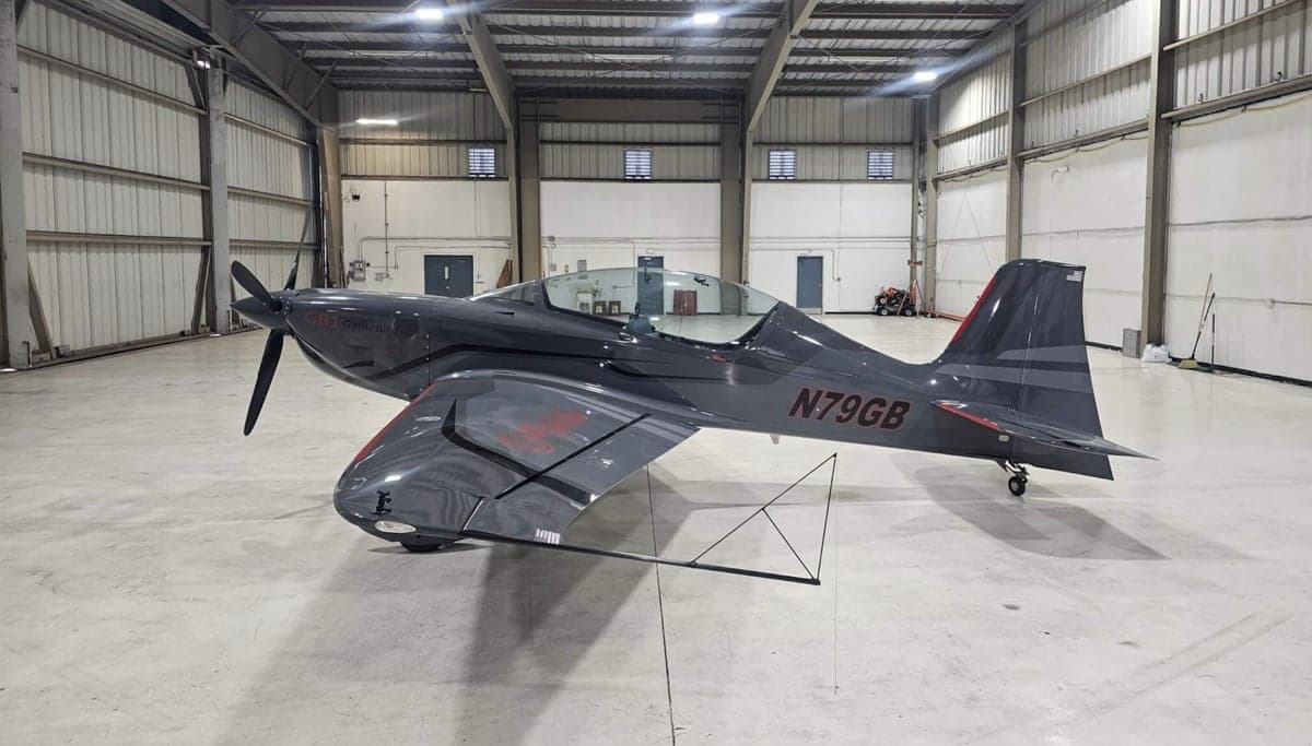 A gray single-engine aircraft is parked inside a hangar.