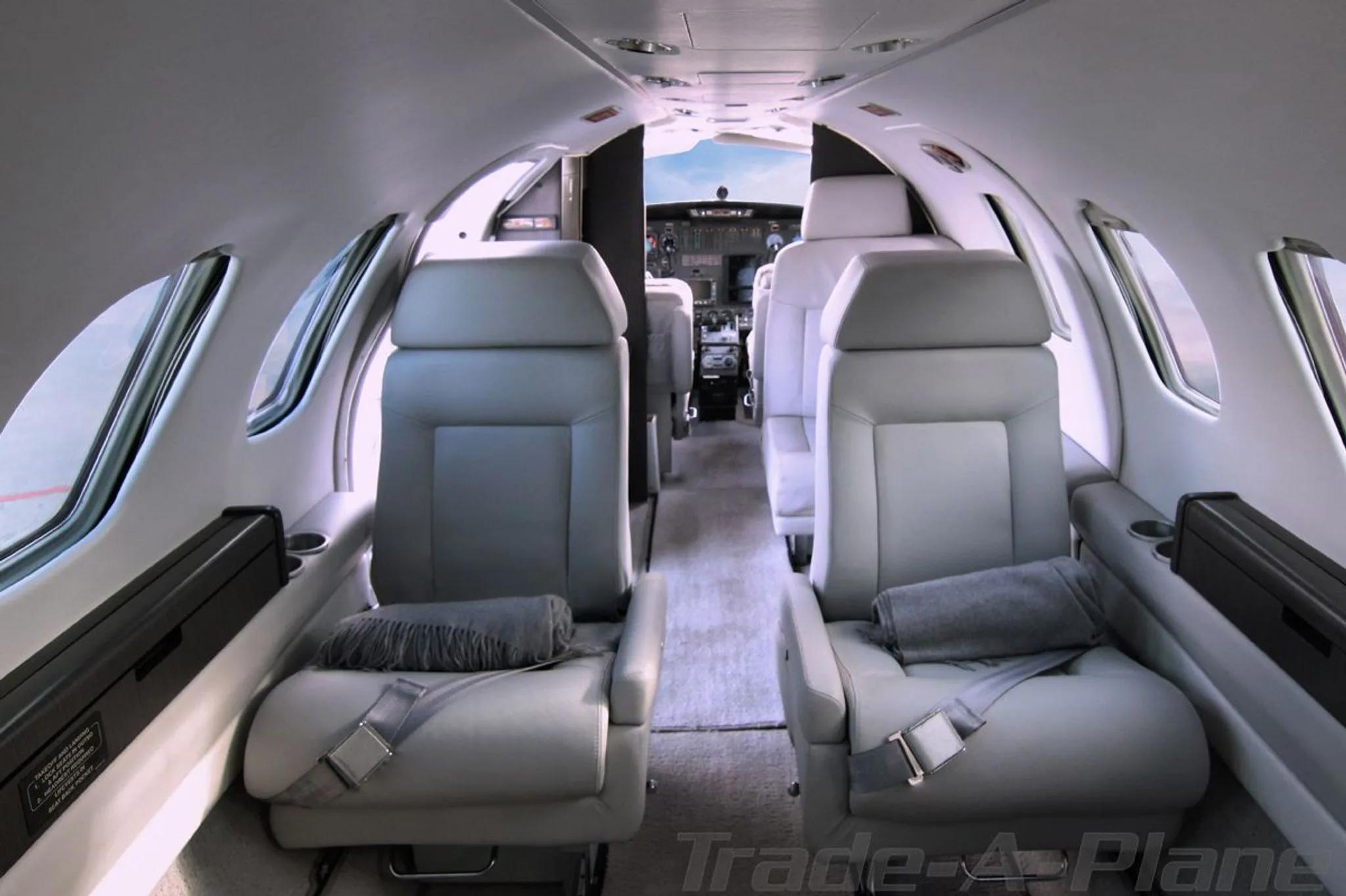 The interior cabin of a Cessna CitationJet with light gray leather seats and a view into the cockpit.