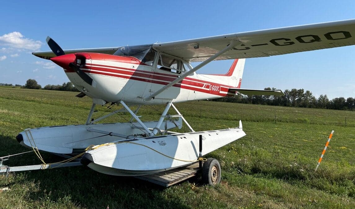 A Cessna floatplane with red and white paint scheme is parked on a grassy field.