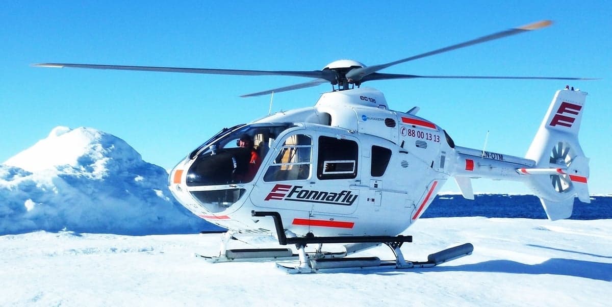 A white EC135 helicopter with red accents sits on a snowy surface.